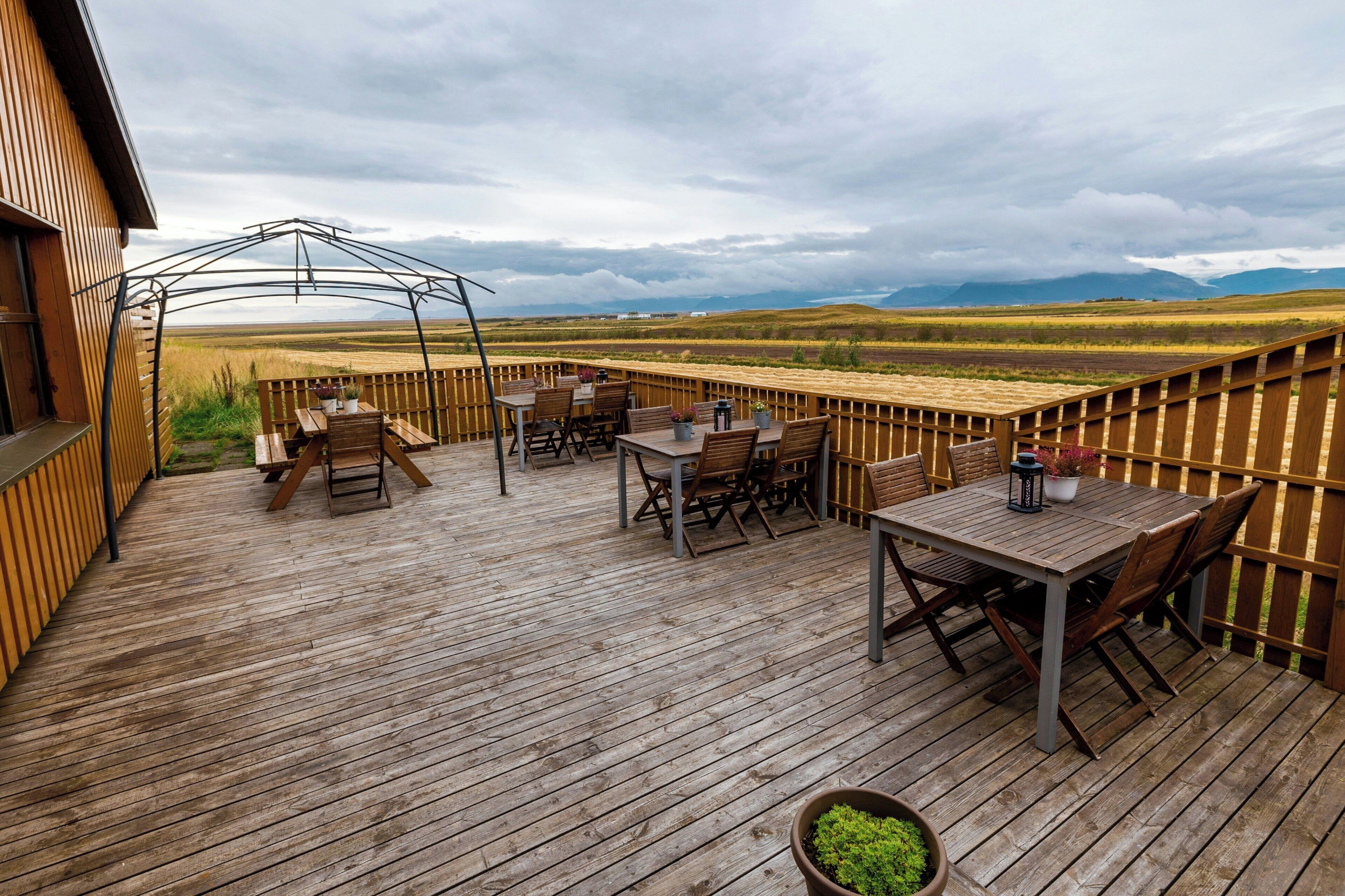 Une terrasse en bois avec des sièges d’extérieur, une pergola et une vue sur un paysage verdoyant avec des montagnes au loin.