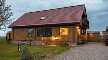 A two-story wooden house with a sloped roof, a front porch, and a gravel driveway.