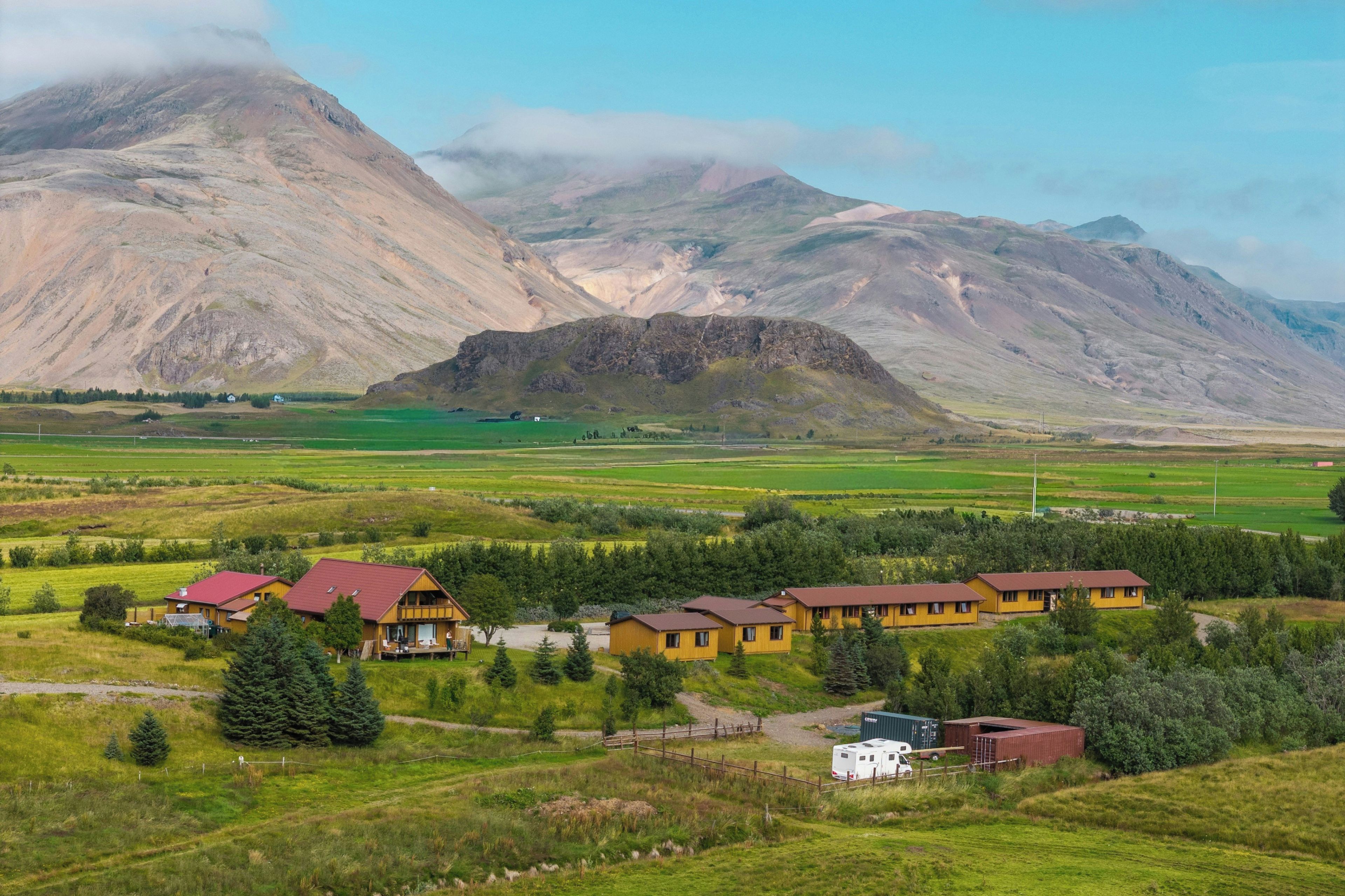 A rural landscape with a row of yellow cabins with red roofs, a white RV, and a small building with a red roof.