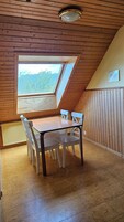 A room with a sloped ceiling, a table with chairs, a window with a view of trees, and a radiator.