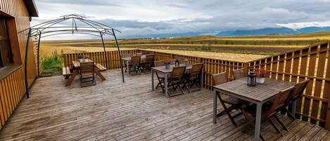 Una terraza de madera con mobiliario exterior, un pérgola y vistas a un paisaje extenso.
