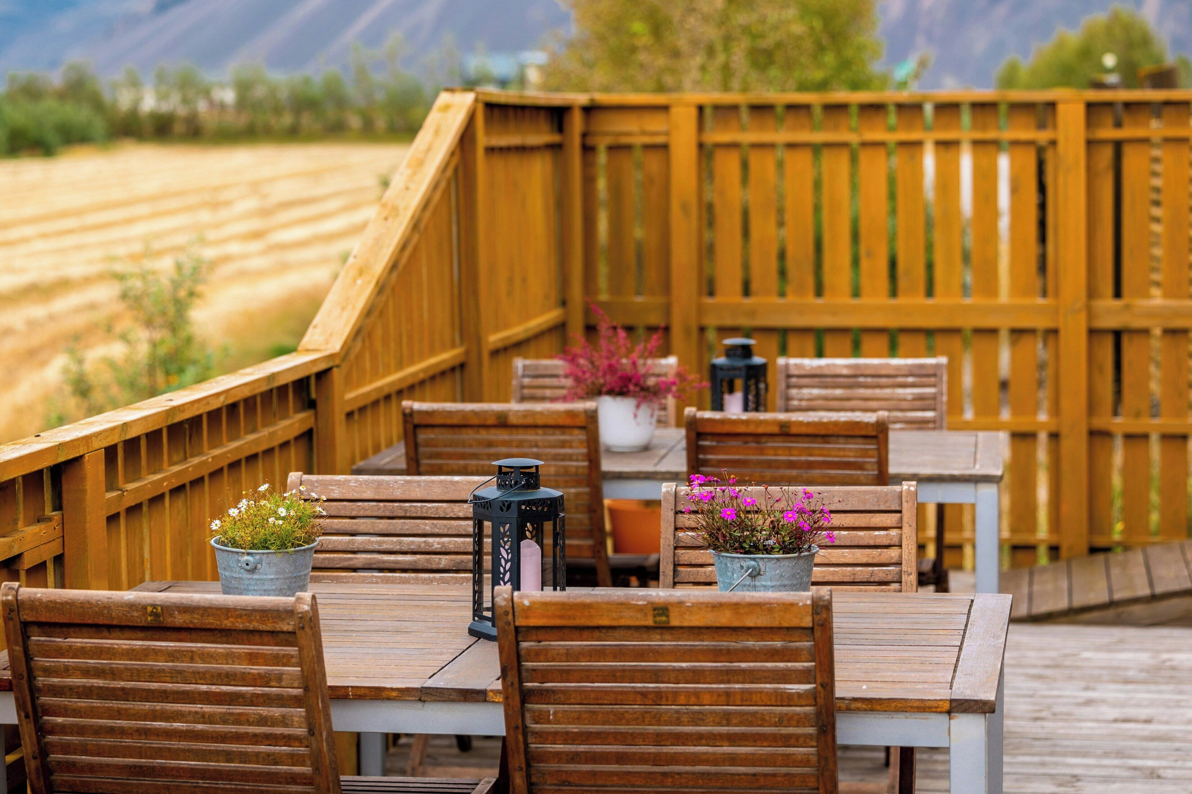 A wooden deck with tables and chairs, potted plants, and lanterns.