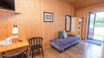 Ein Zimmer mit Holzwänden, einem Bett, einem Schreibtisch mit Lampe, einem Sessel und einem Fernseher.