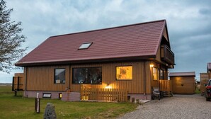 A wooden building with a sloped roof, a visible window, and a gravel driveway. - Arnanes Country Hotel (Höfn)