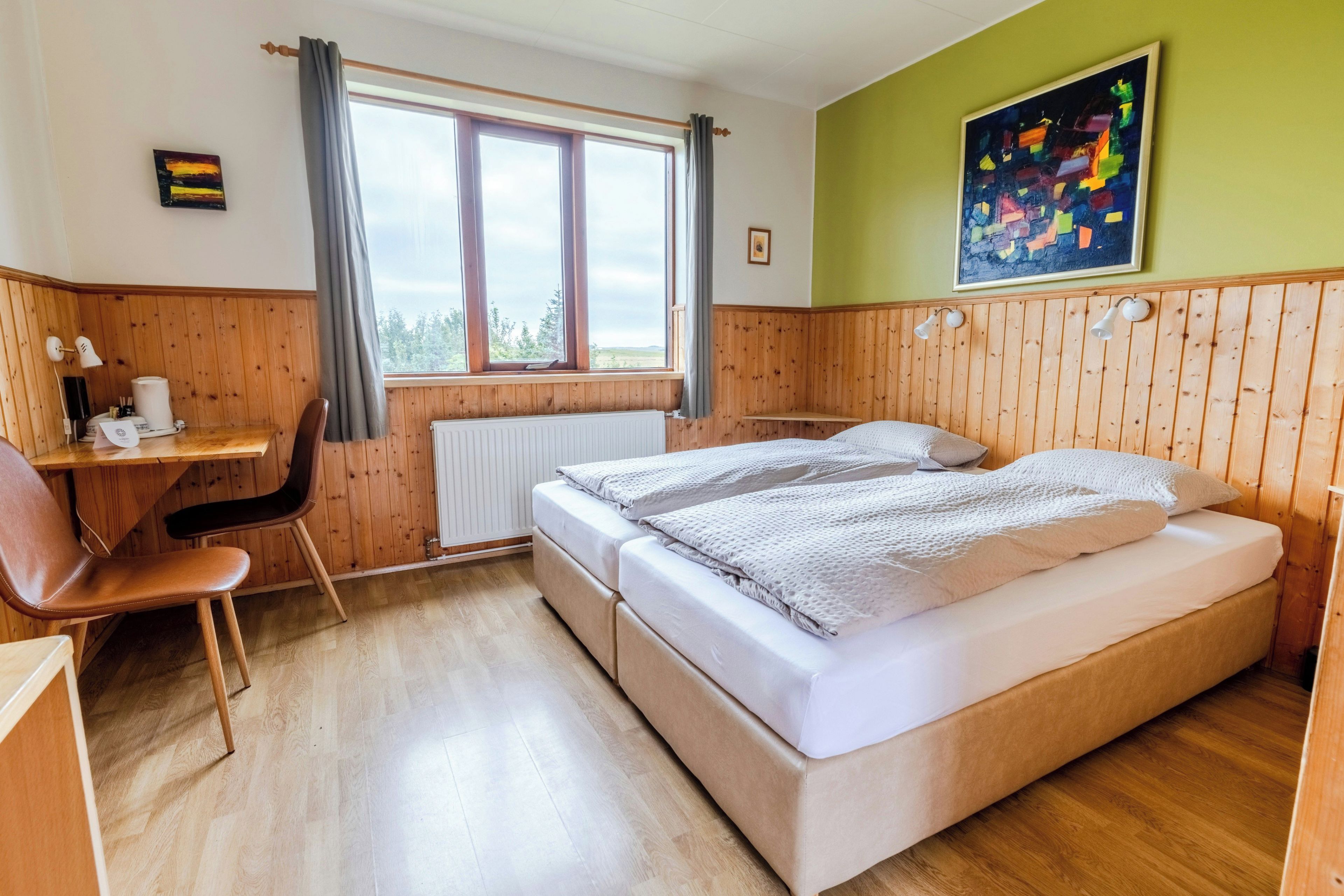 A room with two beds, a desk, a chair, and a window with curtains.