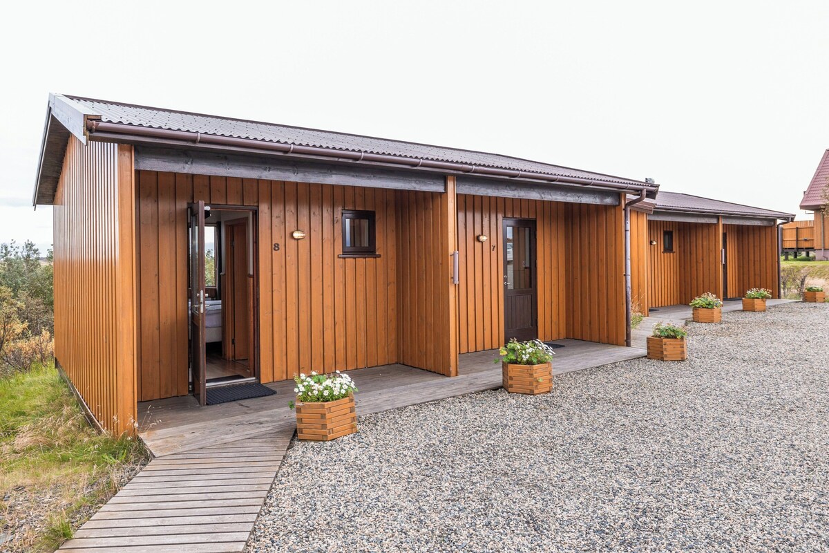 A wooden building with multiple doors and windows, a gravel driveway, and potted plants.