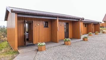 A wooden building with multiple doors and windows, a gravel driveway, and potted plants.