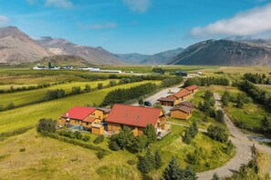 A rural property with multiple wooden cabins, a central building, and a surrounding landscape with mountains and fields. - Arnanes Country Hotel (Höfn)