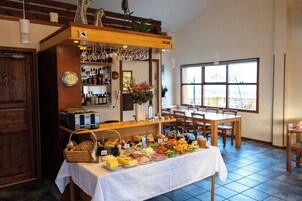 Un bufé de desayuno con gran variedad de alimentos, una zona de bar con copas de vino y vistas al exterior a través de amplias ventanas.