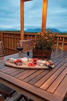 Un tavolo di legno con un tagliere di salumi, un bicchiere di vino rosso e un vaso con fiori gialli.