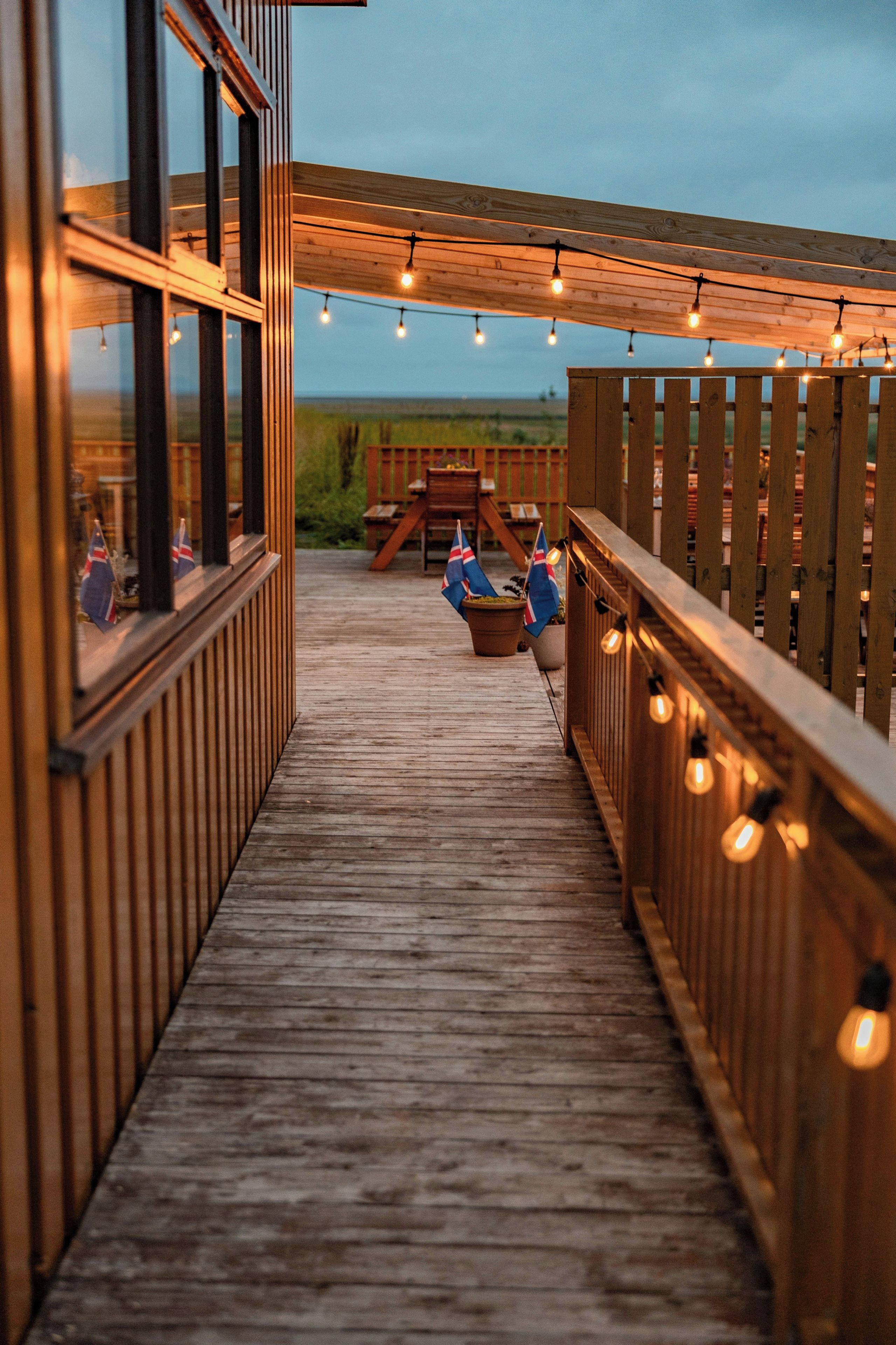 Una terraza de madera con luces de cuerda, una valla de madera y banderas.