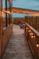 Una terraza de madera con luces de cuerda, una valla de madera y banderas.