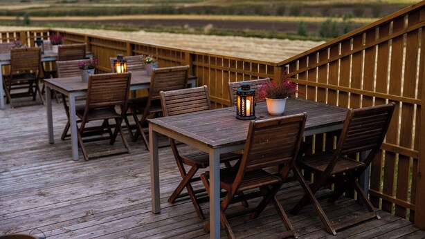 A wooden deck with tables and chairs, a railing, and a view of the landscape. - Arnanes Country Hotel (Höfn)