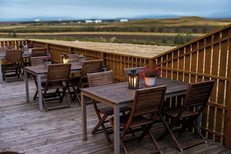 A wooden deck with tables and chairs, a railing, and a view of the landscape.