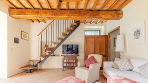 A spacious living area with a wooden staircase, a sofa, ottomans, and a television.
