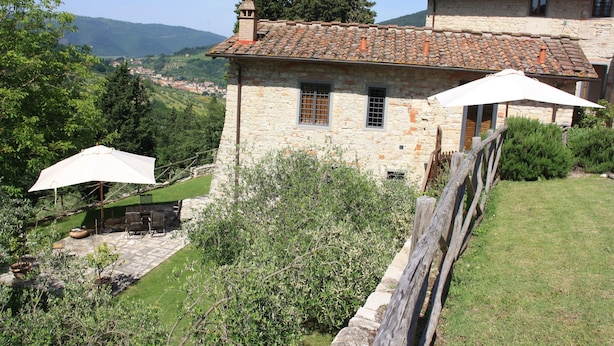 A stone house with a tiled roof, a patio with outdoor furniture, and a view of the surrounding countryside.