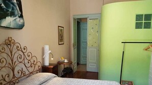 Une chambre à coucher avec un lit, une table de chevet, une chaise, une porte et un mur orné d’un tableau.