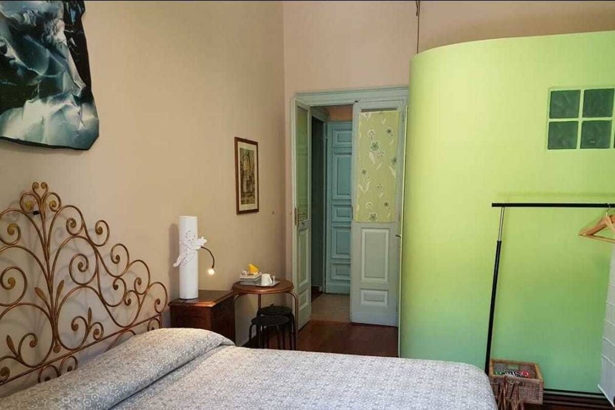 A bedroom with a bed, a bedside table, a chair, a door, and a wall with a painting.