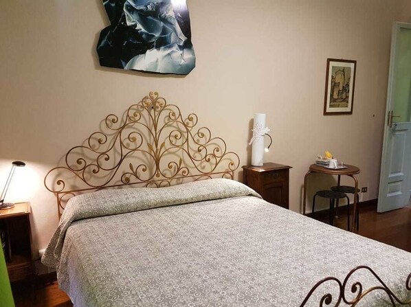 A neatly made bed with a patterned bedspread, a decorative metal headboard, a bedside table with a lamp, and a framed picture on the wall. - B&B La terrazza di San Salvario (Turin)