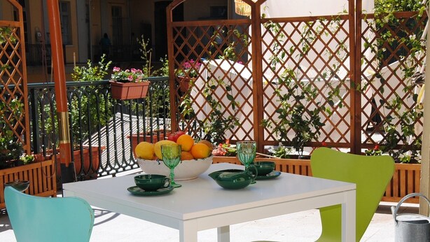 Une table avec un saladier de fruits et des gobelets verts, deux chaises et une chaise en métal.