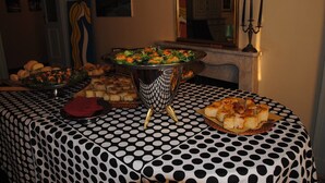 Une table à manger recouverte d’une nappe à pois, un grand saladier en argent et divers aliments, notamment du pain et une salade.