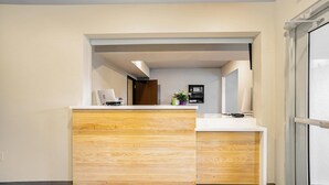 A reception desk with a wooden finish, a white countertop, and a small plant on the counter. - WoodSpring Suites Naples East (Naples)