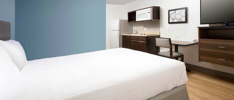 Una habitación de hotel con cama, escritorio, silla, televisión y microondas.