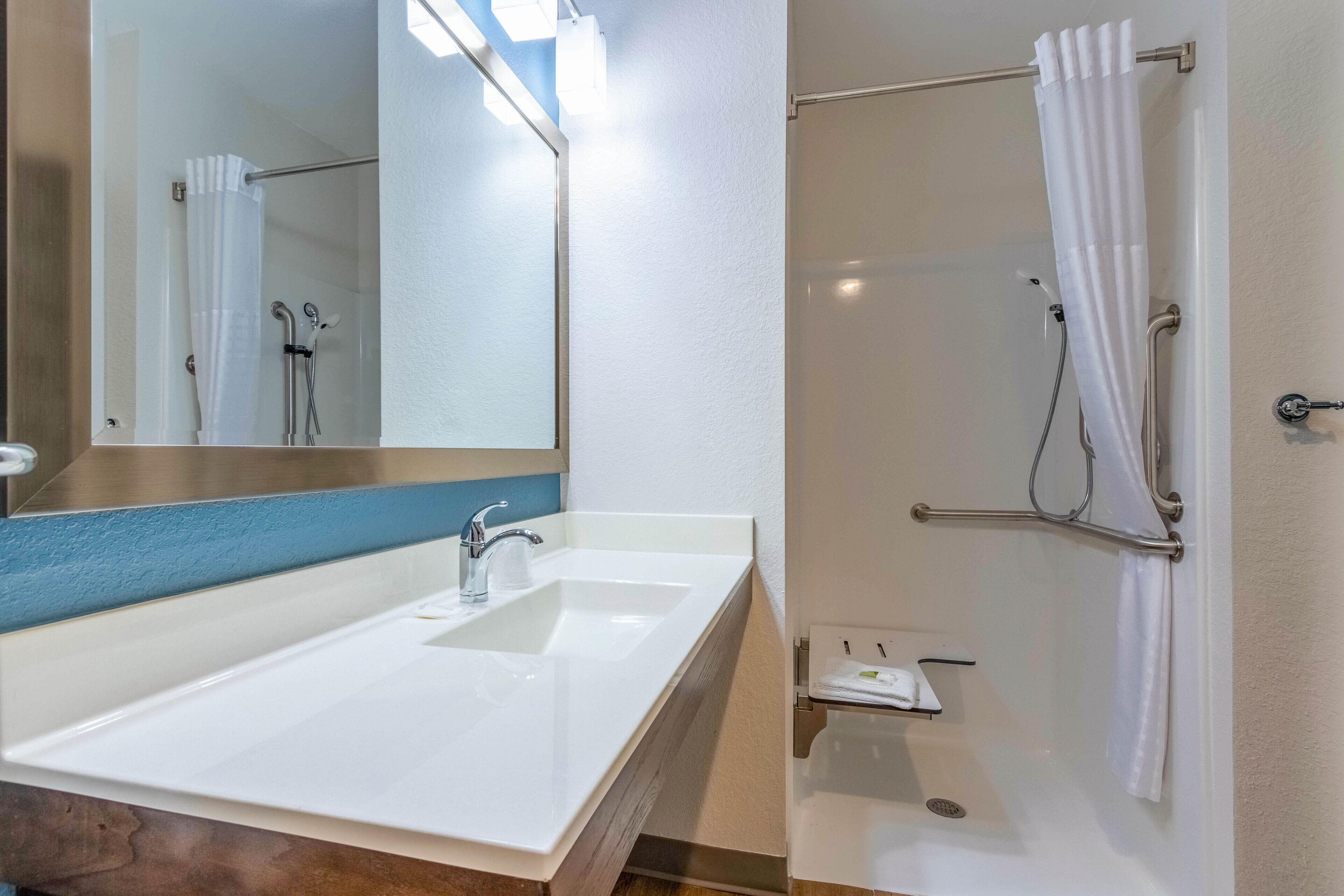 Une salle de bain avec un lavabo blanc, un miroir, une douche avec un rideau blanc et un porte-serviettes.