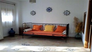 Una habitación con un sofá de estructura metálica, un jarrón azul y placas decorativas en la pared.