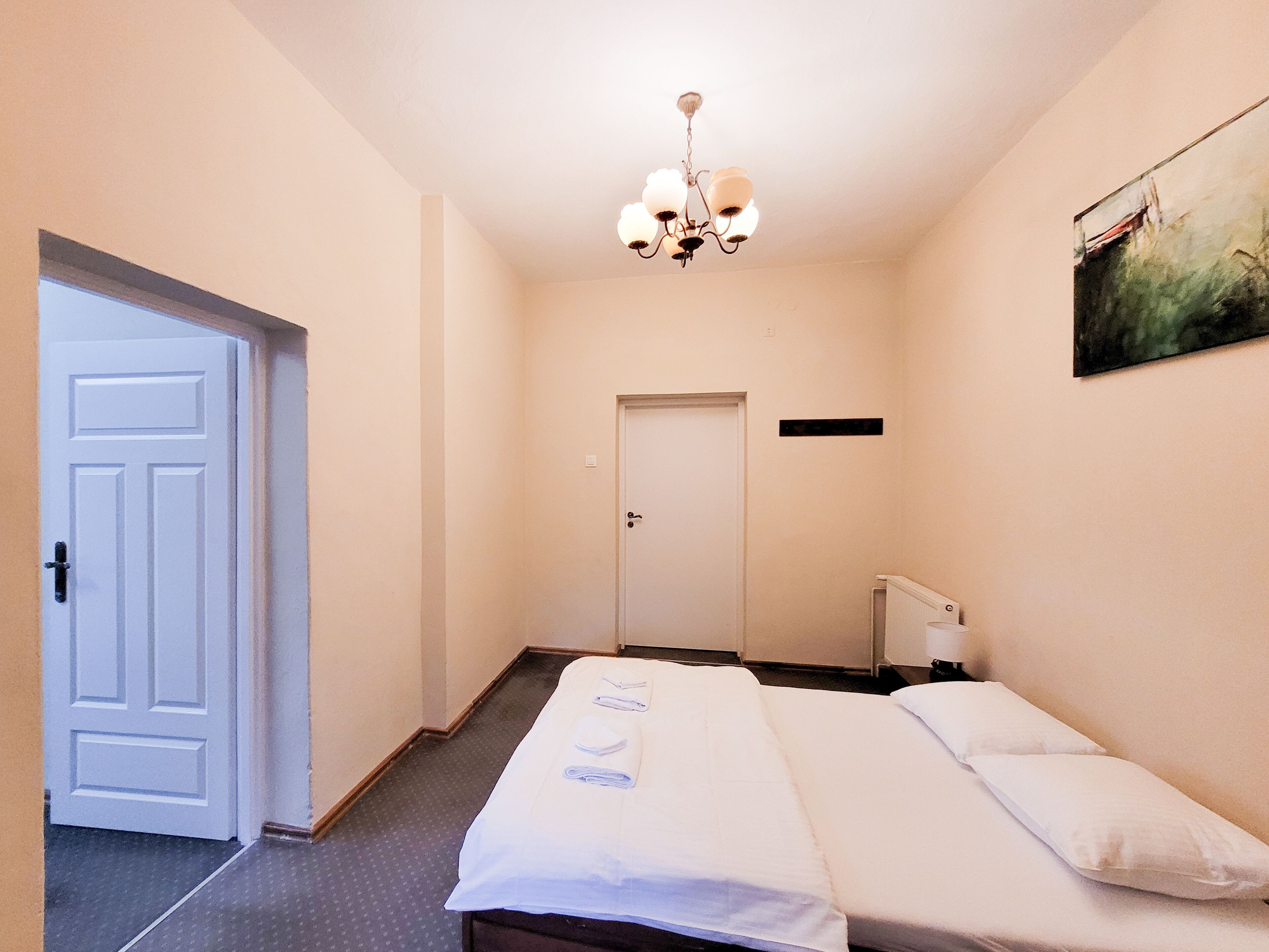 Una habitación de hotel con cama, puerta, radiador y un cuadro en la pared.