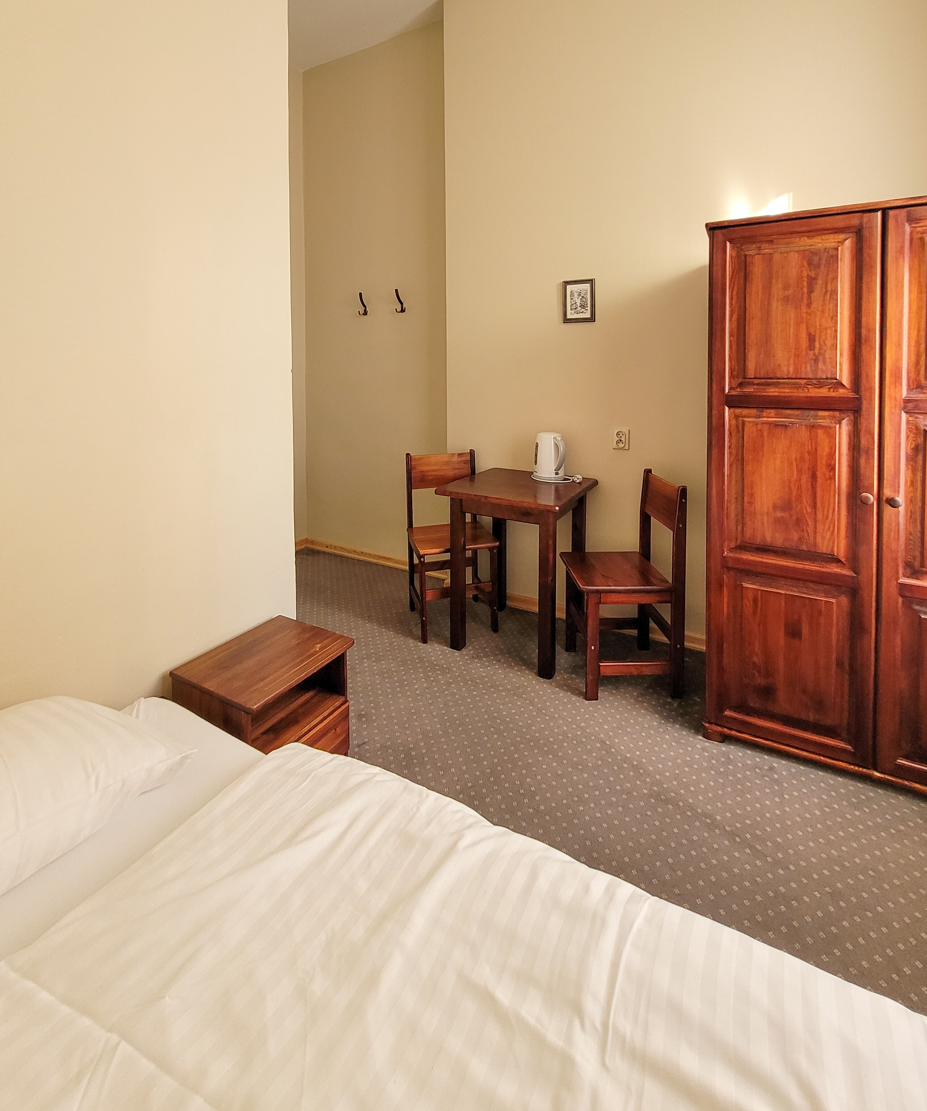 Une chambre d’hôtel avec un lit, une petite table en bois, une bouilloire, deux chaises et une armoire.