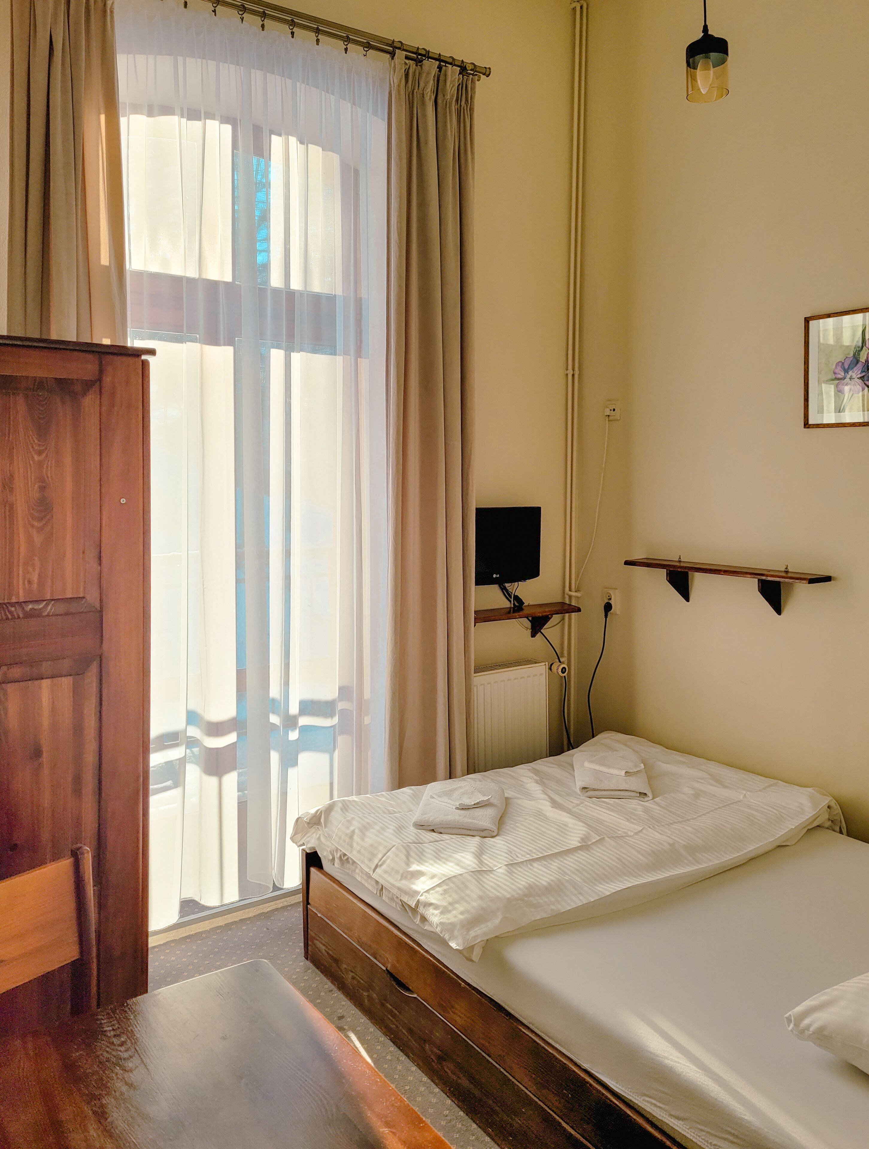 Camera da letto con un letto e un armadio in legno, un termosifone, una TV a parete e una luce a soffitto.