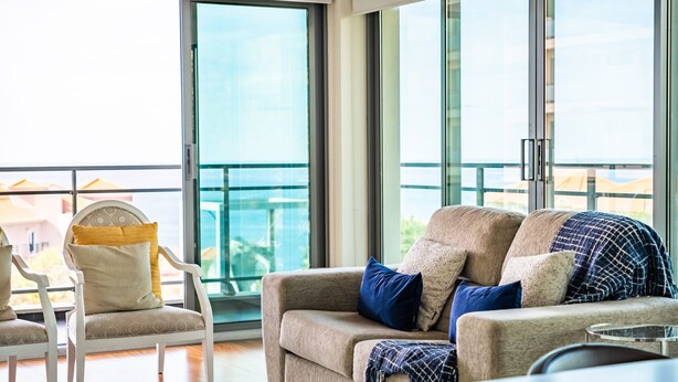 A modern living room with a beige sofa, a white armchair, and a glass balcony door. - Monumental Apartment - By Wehost (Funchal)