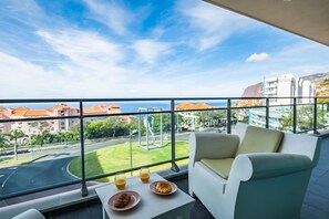 A balcony with a view of the city, a table with croissants and juice, and a white sofa. - Monumental Apartment - By Wehost (Funchal)