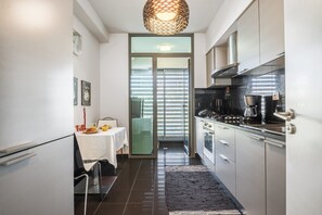 A modern kitchen with a dining area, featuring a black and white color scheme, stainless steel appliances, and a large window with blinds.