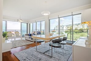 A modern living room with a dining area, large windows, and a view of the city. - Monumental Apartment - By Wehost (Funchal)