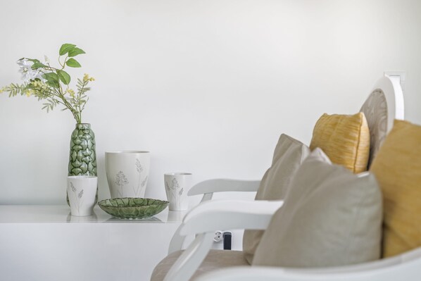 Una mesa blanca con un florero verde, un cuenco blanco y una taza blanca con diseños florales.