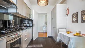 A modern kitchen with stainless steel appliances, a dining area with a table set for breakfast, and a hallway leading to a living space. - Monumental Apartment - By Wehost (Funchal)