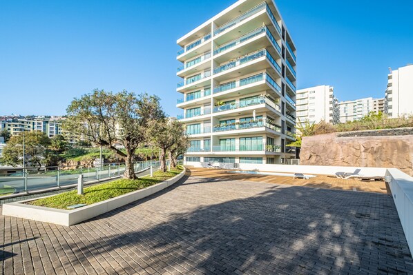 A modern multi-story building with balconies, a paved walkway, and a landscaped area with trees. - Monumental Apartment - By Wehost (Funchal)