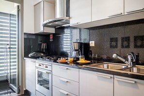 A modern kitchen with stainless steel appliances, a black countertop, and a window with blinds. - Monumental Apartment - By WeHostMadeira (Funchal)