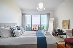 A hotel room with a large bed, a desk, a chair, and a view of buildings through the window. - Monumental Apartment - By Wehost (Funchal)