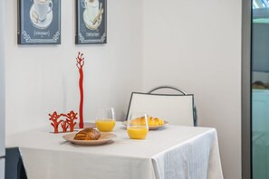 Una mesa de desayuno con cruasanes, jugo de naranja y un plato de comida, frente a una pared blanca con dos cuadros enmarcados.