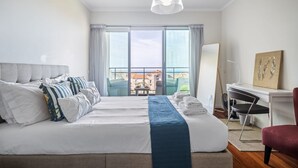 A hotel room with a large bed, a desk, a chair, and a view of buildings through the window. - Monumental Apartment - By Wehost (Funchal)