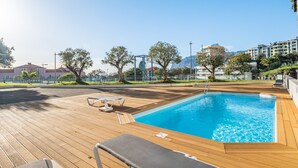 A swimming pool with wooden deck, lounge chairs, and a clear view of surrounding buildings and trees. - Monumental Apartment - By Wehost (Funchal)