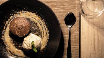 Un plato con un brownie y helado, una cuchara y un vaso de agua sobre una mesa de madera.