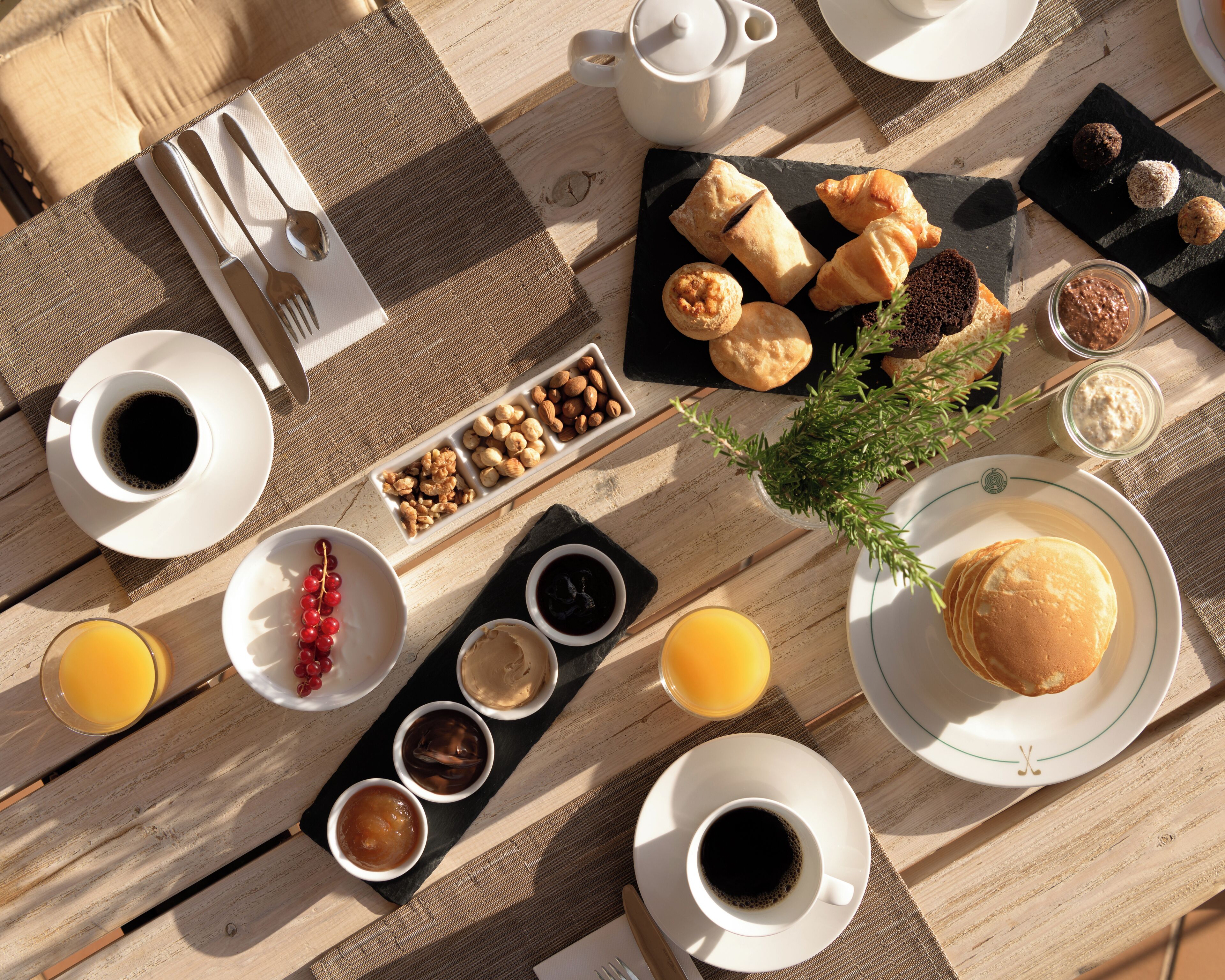 Une table en bois dressée pour le petit-déjeuner, avec une variété de plats et de boissons.