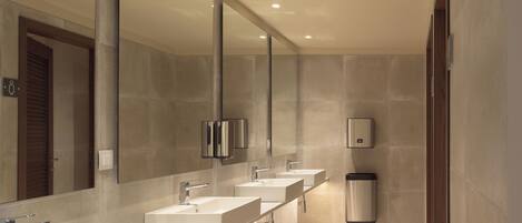 A modern bathroom with three sinks, a large mirror, and a hand dryer.