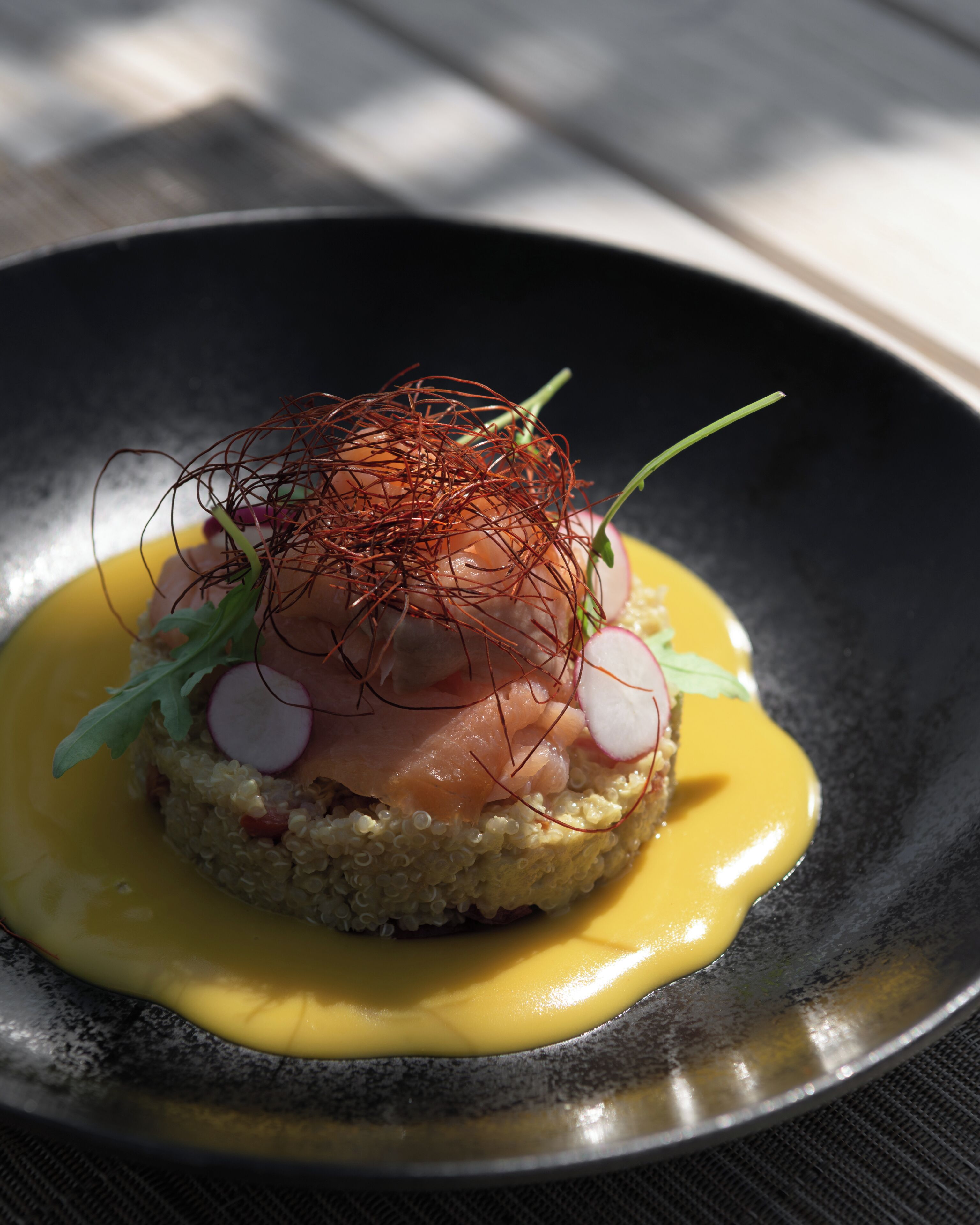 A dish with salmon, radish, and a yellow sauce on a plate.