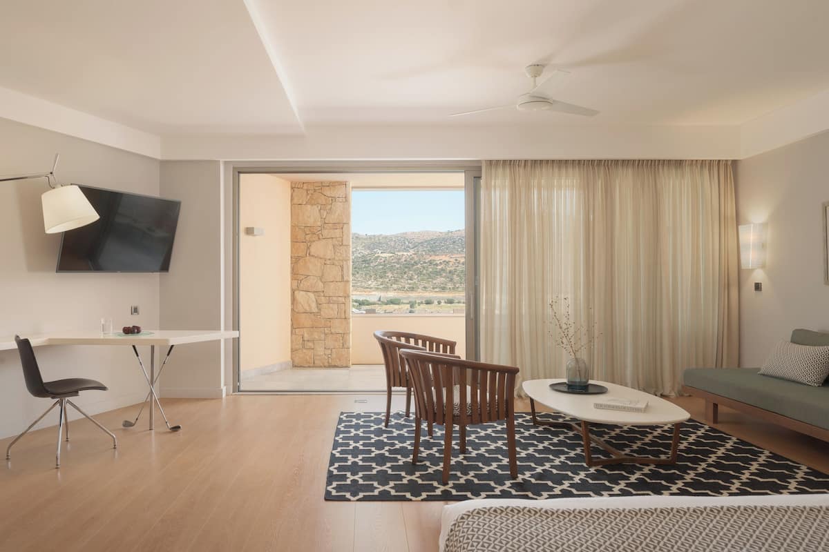 A modern hotel room with a dining area, a sofa, a TV, and a view of the outdoors.