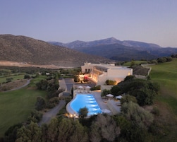 A modern hotel with a swimming pool, surrounded by greenery and mountains.